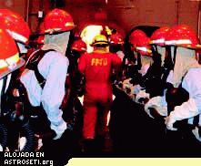 <i>Un instructor anti-fuegos encabeza bomberos para atacar un fuego Clase Bravo (alimentado por petróleo) durante una sesión de entrenamiento militar. Tanto la NASA como los militares pusieron mucho énfasis en estar preparados para varios riesgos por fuego, tanto en Tierra como en el espacio.</i>