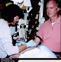 <i>Con el fin de prepararse para los experimentos en ciencia de la vida durante la misión STS-107, la astronauta Dra. Laurel Clark extrae sangre del voluntario y astronauta sustituto John Charles, científico de misión para los experimentos OBPR en el vuelo del Columbia en julio.</i>