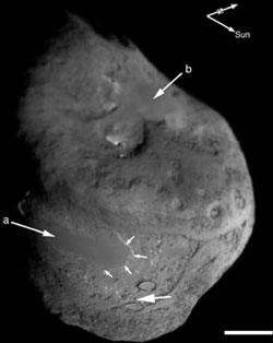 Flechas a y b señalan las regiones planas y grandes. El lugar de impacto está indicado por la tercera flecha grande. Las flechas pequeñas resaltan el escarpado que es brillante debido al ángulo de iluminación, el cual muestra el área plana y elevada sobre el terreno extremadamente rugoso. La barra de escala representa un kilómetro y las dos flechas arriba del núcleo apuntan hacia el sol y el eje de rotación del núcleo. El norte celeste está cerca del polo de rotación.
<i>Créditos: NASA/JPL/UMd</i>