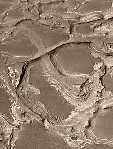 Una región próxima al borde sudeste del abanico muestra canales invertidos a diferentes niveles en el interior del depósito sedimentario, lo cual indica una larga y compleja historia de procesos relacionados con el agua. Una cresta cruza sobre otra justo a la izquierda del centro de este recuadro. La parte alta de la cresta inferior es el antiguo fondo de un canal que transportaba agua y sedimentos hacia el más bajo de la derecha. La parte alta de la cresta superior fue una vez el suelo de un canal que movía material hacia el entronque de la derecha o al de arriba y derecha. La cresta más baja es el canal más antiguo. Fue completamente rellenado y enterrado bajo la superficie cuando se formó el canal superior. Crédito de la Imagen: JPL/MSSS
