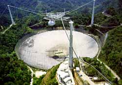 El radio telescopio de Arecibo es actualmente el telescopio más grande de un solo plato en el mundo para radio astronomía. En 1974, Arecibo fue utilizado para transmitir un <a href=http://www.seti-inst.edu/science/a-message.html target=_blank>mensaje</a> de la Tierra a un grupo de estrellas en M13.
"A diferencia de nuestros colegas radio astrónomos, no podemos depender de señales que puedan ser escuchadas a través de todo el disco radial. Tales emisiones de banda ancha, del tipo de las emitidas hacia el espacio por transmisores naturales cósmicos (como quásares) no son muy afectadas por la interferencia terrestre: la selva de señales que brotan del radar local, satélites GPS, pájaros de telecomunicación, etc., . No nos preocupamos por tratar de identificar si estas señales son satélites espías o radares de aeropuertos sin importancia.
Los anotamos y nos olvidamos”.- <a href=http://www.astrobio.net/news/modules.php?op=modload&name=News&file=article&sid=668 target=_blank>Seth Shostak</a>. Crédito: NAIC - Observatorio Arecibo