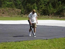 Grandes lonas alquitranadas son desplegadas en el Centro Espacial Stennis para comprobar la precisión de los satélites comerciales de observación. Los empleados del Centro Stennis visten calcetines para asegurarse de no marcar ni dañar las lonas, y emplean ventiladores eléctricos para eliminar los restos. Propietario de la imagen: NASA