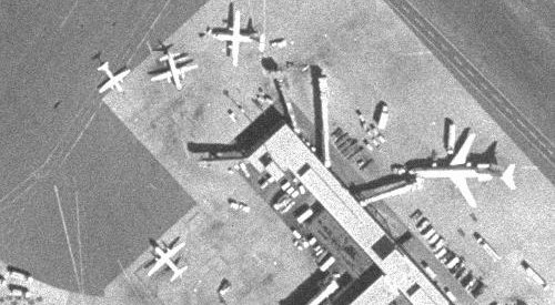 Un ejemplo de una fotografía de medio metro de resolución tomada desde arriba, de la misma resolución que serán las imágenes de la LROC. Esta fotografía de un aeropuerto muestra aviones de varias dimensiones así como vehículos del tamaño de coches. Nótese cómo las sombras ayudan a que los objetos resalten del fondo. Las imágenes de alta resolución de la LROC también serán en escala de grises, pero estarán menos granulosas que el ejemplar de arriba gracias a su tecnología de imágenes digitales.
<i>Imagen cortesía del <a href= http://ortho.mit.edu/ target=_blank><u>Proyecto Digital Ortofoto del MIT</u></a>.</i>