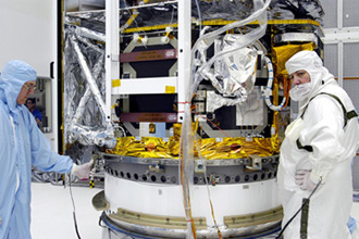Trabajadores procesan la Instalación del Telescopio Infrarrojo Espacial, el cual permanecerá en la sala limpia hasta su retorno a la plataforma a comienzos de Agosto.
